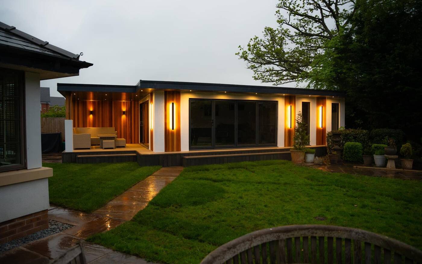 An Elevate garden room lit up at dusk in a North West garden